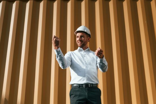 Standing against yellow background. Male worker is on the location with containers